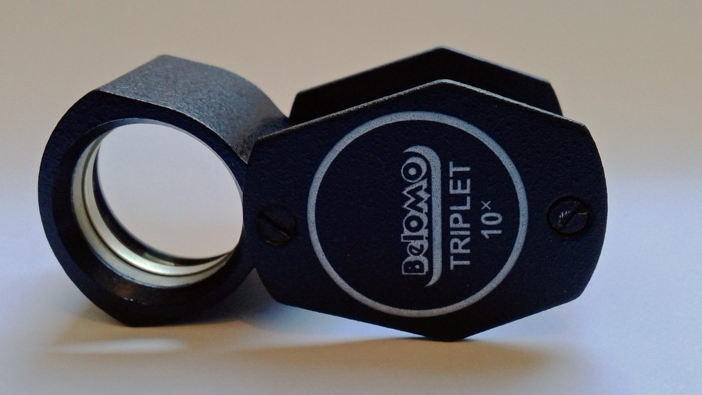 A 10x achromatic triplet jeweller's loupe, open, on a dark surface