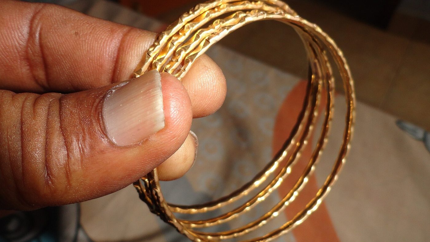 A hand holding a set of four traditional Indian gold bangles