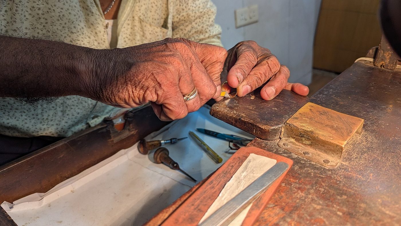 A traditional goldsmith hand-engraving a gold ring at his bench in Goa, India