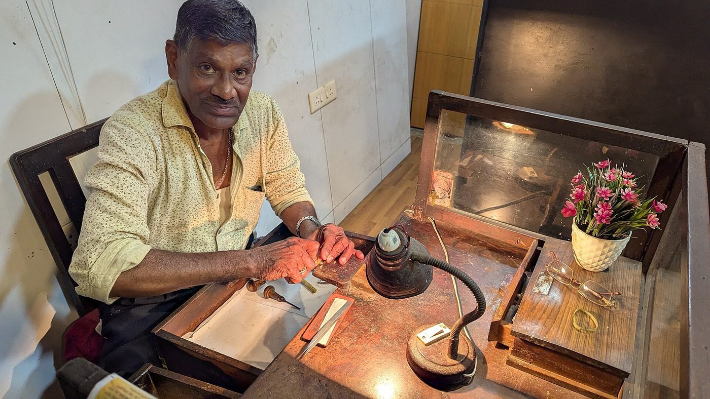 A traditional goldsmith working at his bench with a lamp in Margao, Goa